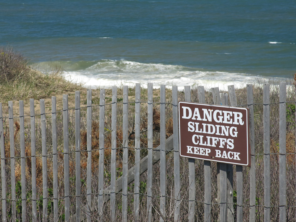 Danger sign on fence above eroded beach on Cape Cod