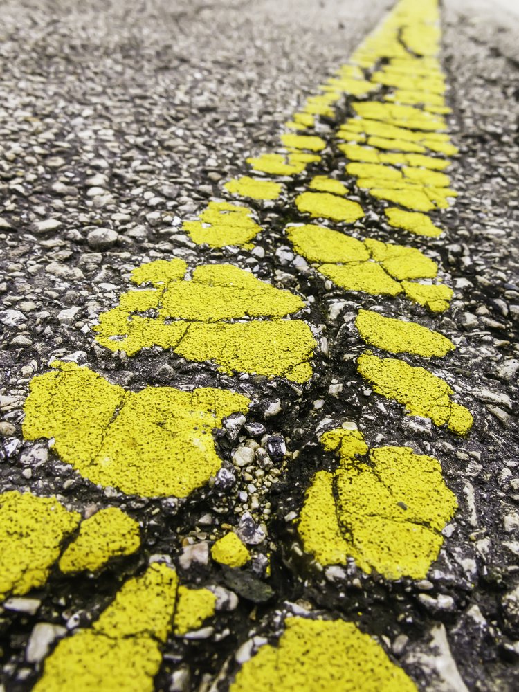 Fragmentation and time Breakup of yellow center line on old asphalt road (shallow depth of field)